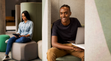 Two students use devices while studying in quiet booth seating areas on campus.