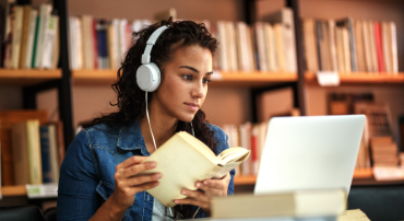 A student looking at a laptop screen while holding an open book