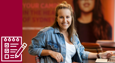 A student sits propped on a chair, working on her laptop, with a relaxed expression.